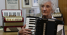 Maria Brückl am Akkordeon; im Hintergrund sind weitere Instrumente und eine Urkunde zu sehen