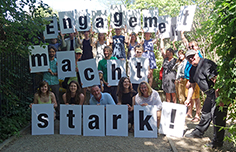 Gruppenbild mit Menschen, die Schilder mit Buchstaben in die Höhe halten; zu lesen ist: Engagement macht stark!