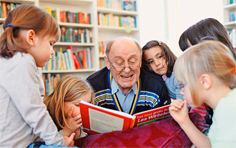 Älterer Mann liest vielen Kindern etwas vor